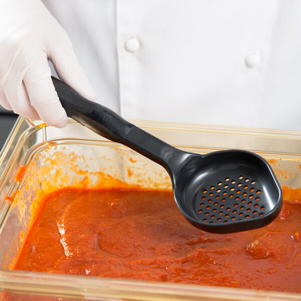 A gloved hand using a black Vollrath Spoodle to serve red sauce.