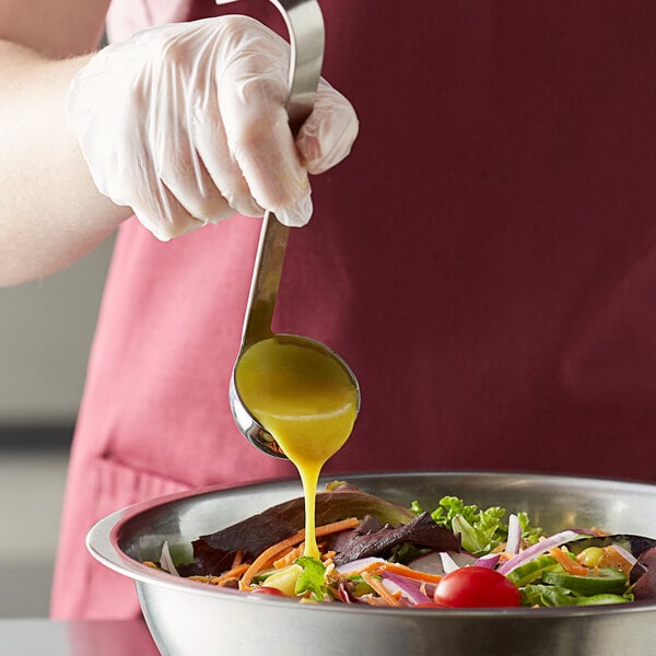 A person using a Vollrath stainless steel ladle to pour yellow dressing onto a salad.