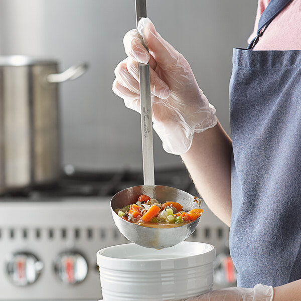 A person holding a Vollrath stainless steel ladle with food in it.