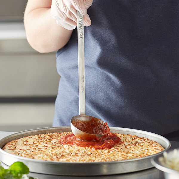 A stainless steel Vollrath ladle with red sauce in it over a plate of food.