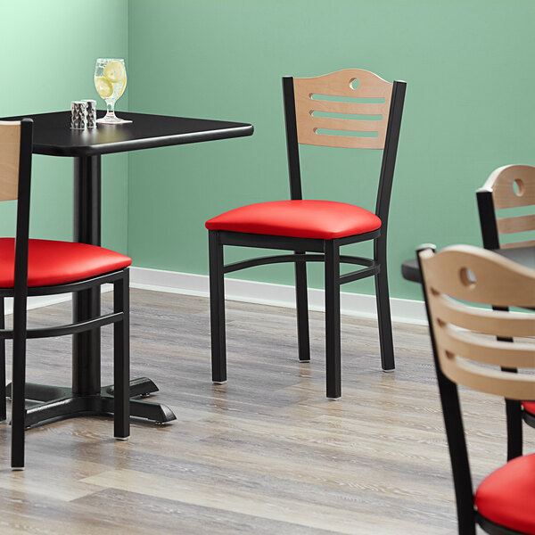 A Lancaster Table & Seating black bistro chair with a red vinyl seat and natural wood back in a restaurant dining area.
