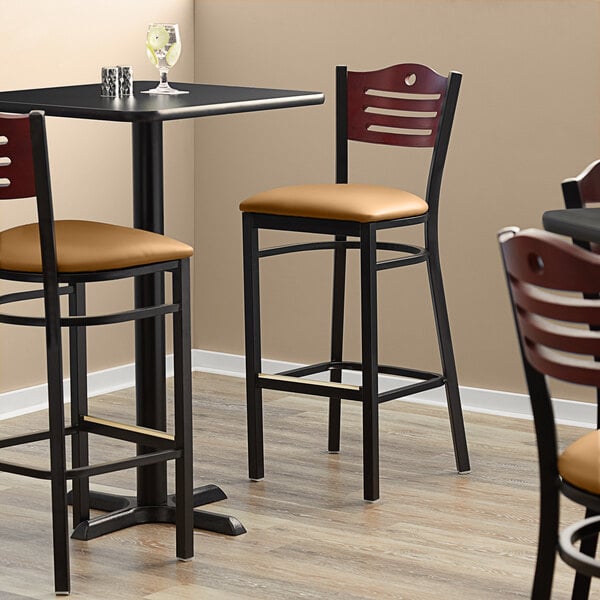 A Lancaster Table & Seating black bistro bar stool with mahogany wood back and light brown vinyl seat detached.