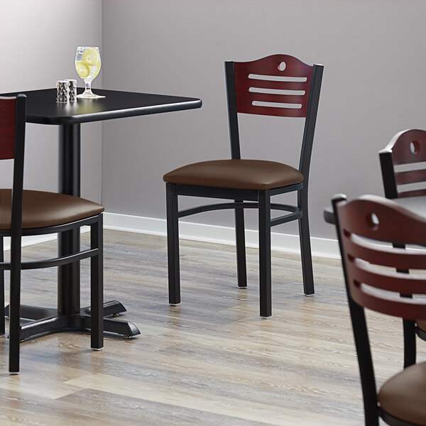 A Lancaster Table & Seating mahogany wood and black metal bistro chair with a dark brown vinyl seat on a table in a restaurant dining area.