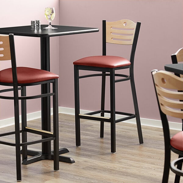 Three Lancaster Table & Seating bistro bar stools with burgundy seats and natural wood backs on a table in a restaurant.