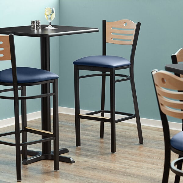 A Lancaster Table & Seating Bistro Bar Stool with a navy blue vinyl seat on a table in a restaurant dining area.