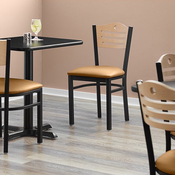 A black Lancaster Table & Seating bistro chair with a light brown vinyl seat and natural wood back.