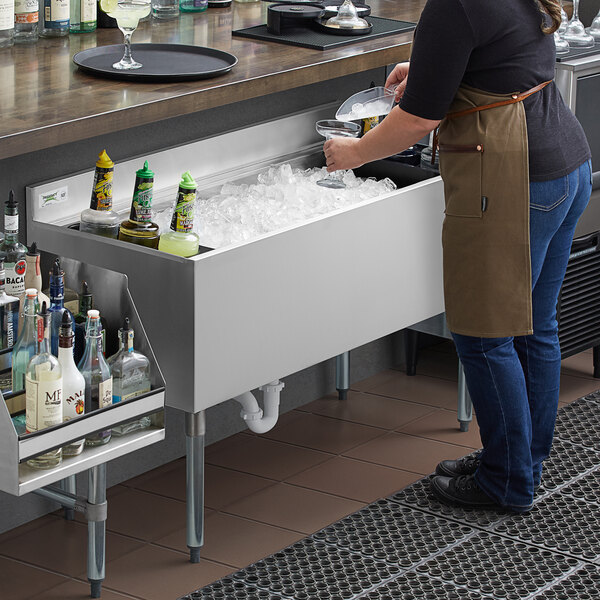 A woman wearing an apron pours ice into a Regency underbar ice bin on a counter.
