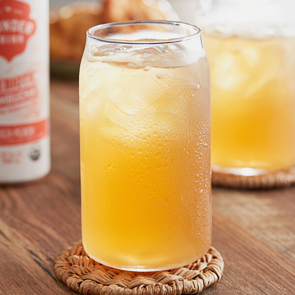 A glass of Wonder Drink Organic Ginger Peach Kombucha with ice on a white background.