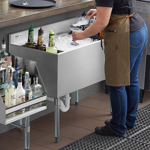 A person putting bottles in a Regency stainless steel underbar ice bin on a counter in a cocktail bar.