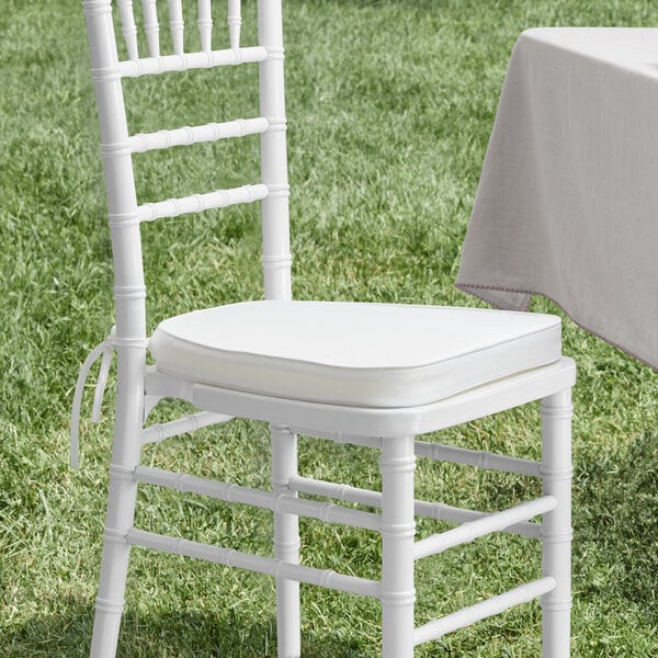 A white Lancaster Table & Seating Chiavari chair with an ivory cushion tied to it.
