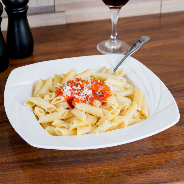 A plate of pasta with sauce in a CAC white square porcelain pasta bowl with a fork on the plate.