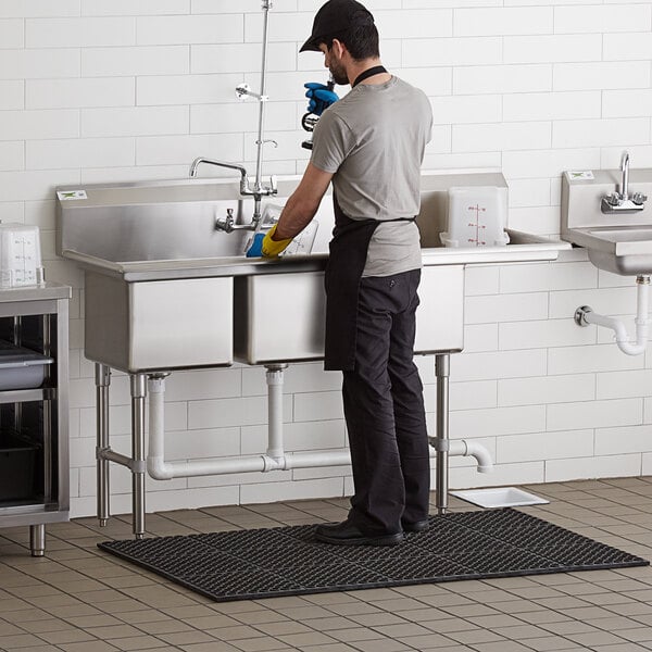A man standing in a Regency stainless steel 3 compartment sink with a drainboard.
