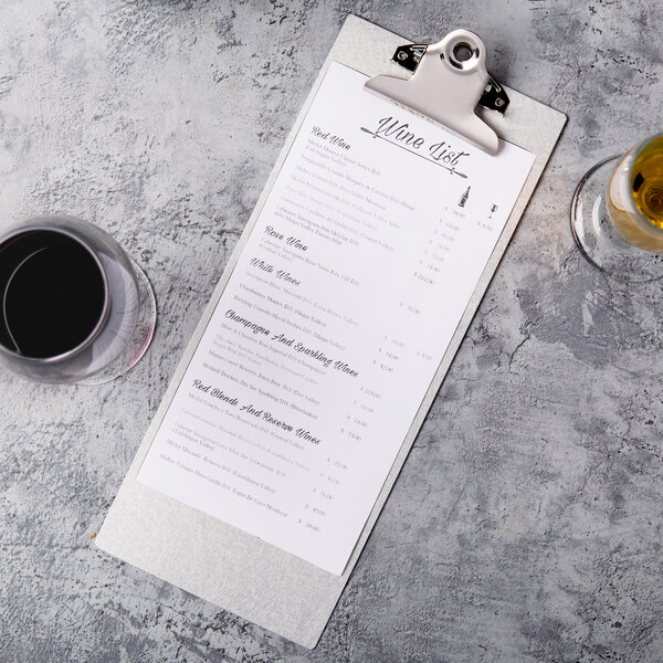 A Menu Solutions Alumitique clipboard holding a menu on a table with a glass of wine.