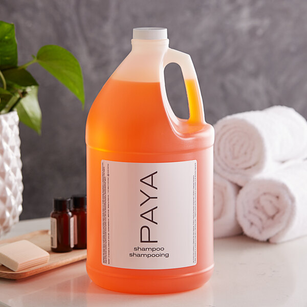 A PAYA Papaya shampoo jug on a counter next to towels and a plant.