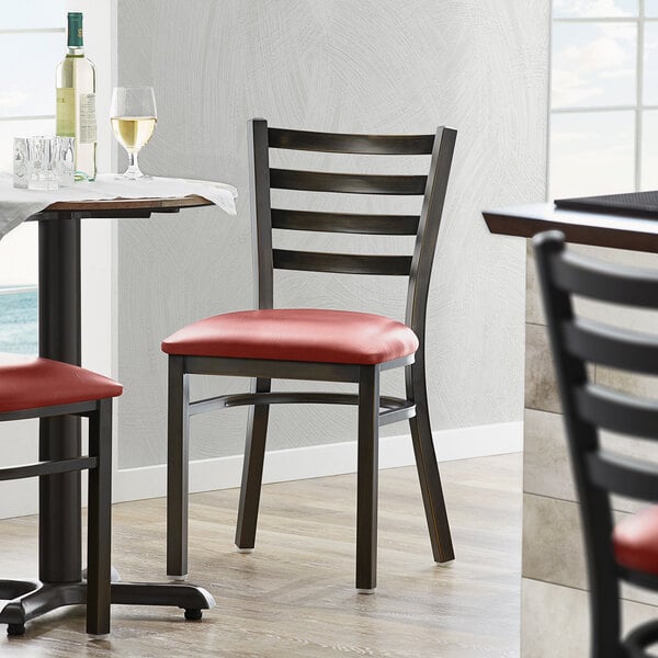 A Lancaster Table & Seating distressed copper ladder back chair with a burgundy cushion on a table in a restaurant dining area.