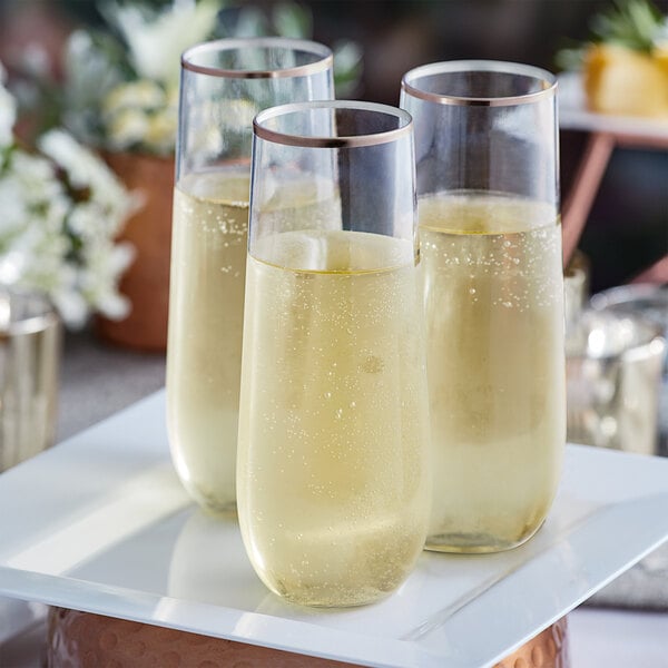 Two Visions clear plastic stemless champagne flutes with rose gold rims filled with champagne on a white plate.