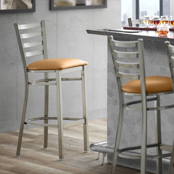 A Lancaster Table & Seating ladder back bar stool with a light brown vinyl padded seat.