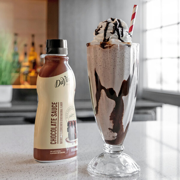 A glass of chocolate milkshake with a straw next to a bottle of DaVinci Gourmet Chocolate Flavoring Sauce.
