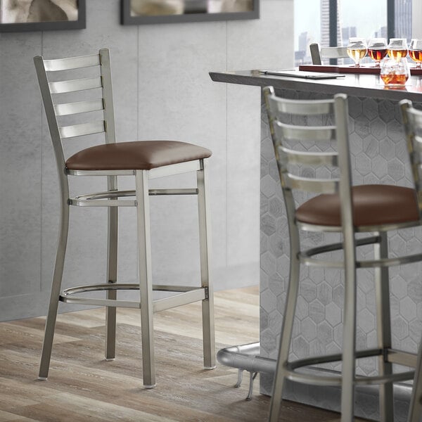 A Lancaster Table & Seating ladder back bar stool with a dark brown vinyl padded seat.