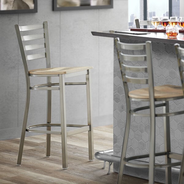 A Lancaster Table & Seating clear coat finish ladder back bar stool with a driftwood seat next to a counter.