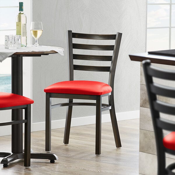 A Lancaster Table & Seating distressed copper ladder back chair with a red vinyl padded seat at a table in a restaurant.
