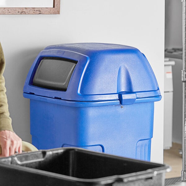 A man using a blue Toter square dome lid to cover a black 50 gallon slimline trash can.