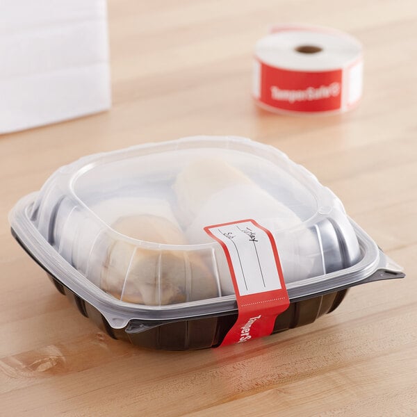 A plastic container with a roll of red paper labels with white TamperSafe text on it.