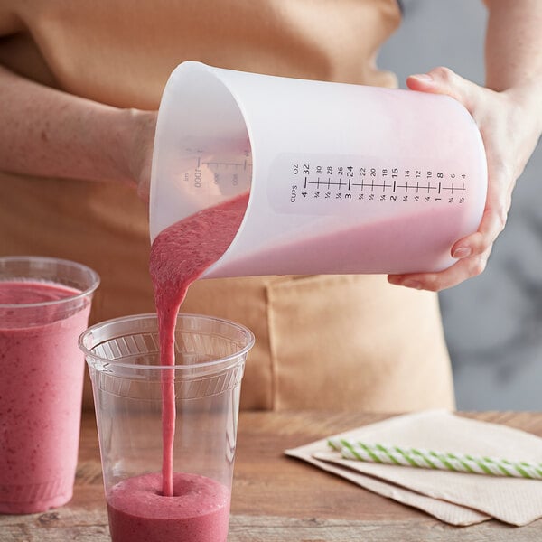 A woman pouring a pink smoothie into an iSi translucent silicone measuring cup.