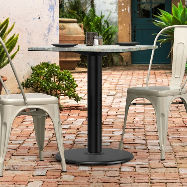 A Lancaster Table & Seating Excalibur outdoor table base with chairs on a brick patio.