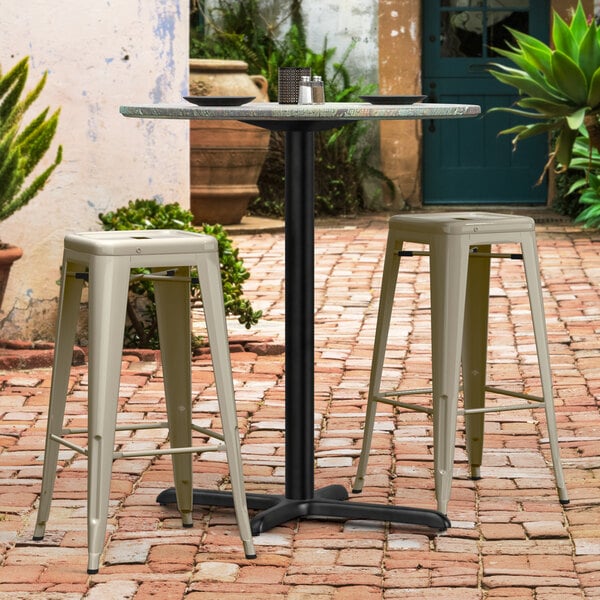 A Lancaster Table & Seating Excalibur outdoor table with bar stools on a brick patio.