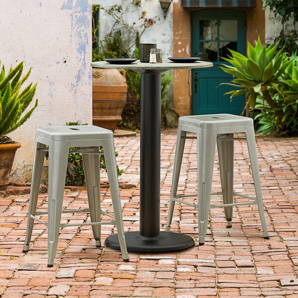 A Lancaster Table & Seating black outdoor table base with stools on a brick patio.