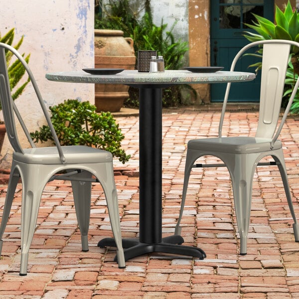 A Lancaster Table & Seating black outdoor table base with a table and chairs on a brick patio.
