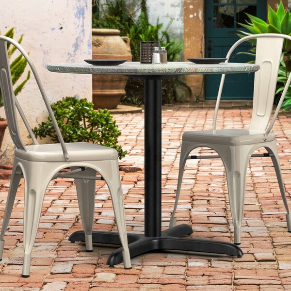 A Lancaster Table with a black Excalibur table base on a brick patio with two white chairs.