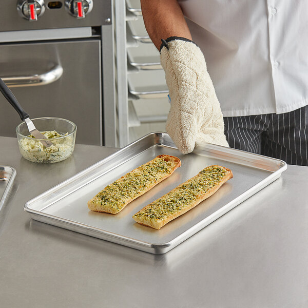 A person in a chef's uniform using a Vollrath bun pan to bake long rectangular bread with cheese on it.