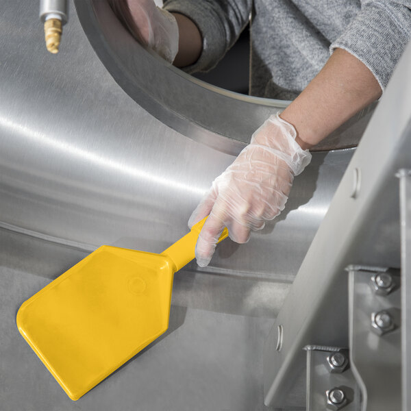 A person in gloves using a yellow Carlisle Sparta nylon paddle blade to clean a metal cylinder.