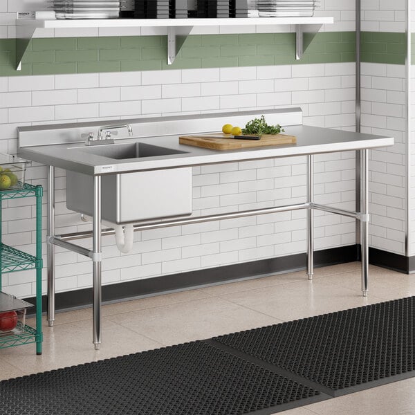A stainless steel work table with an integrated sink, cross brace support, and a cutting board with food items on top.