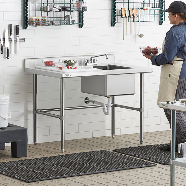 A woman standing in a professional kitchen using a Regency stainless steel work table with a sink.