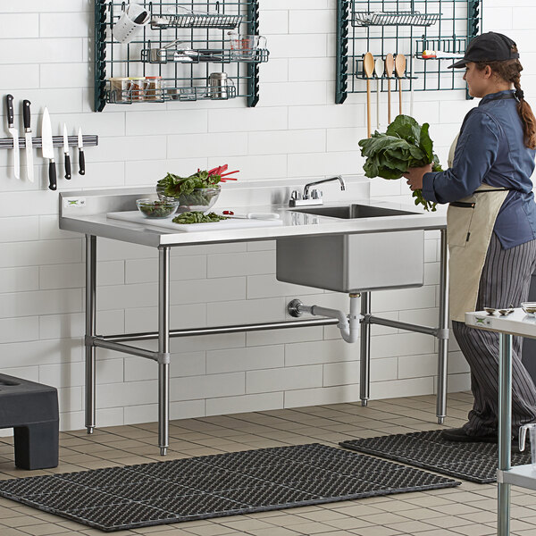A woman using a Regency stainless steel work table with a sink in a professional kitchen.