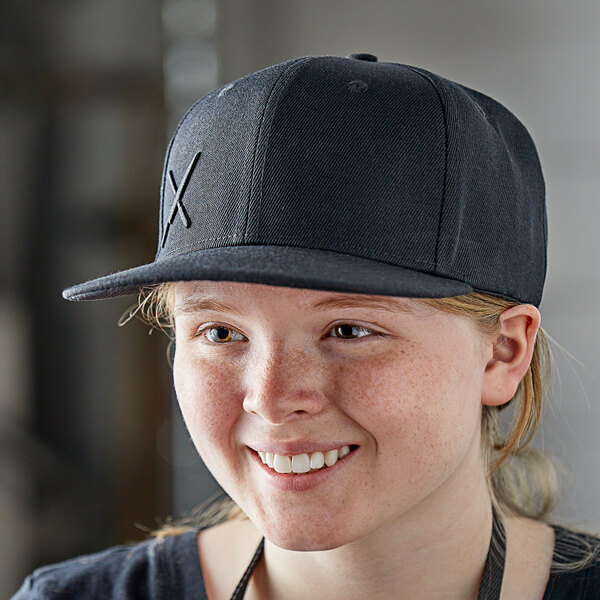 A woman wearing a black Mercer Culinary snapback hat with a small black logo.