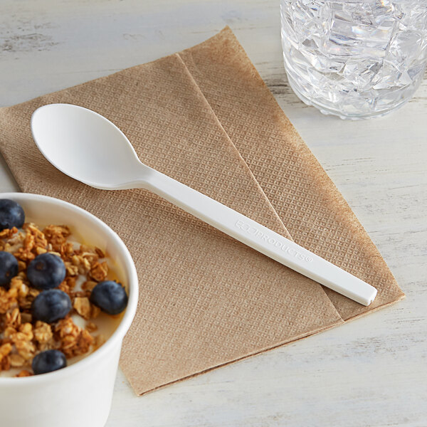 A bowl of cereal with blueberries and an Eco-Products renewable plant starch spoon on a table with a napkin.