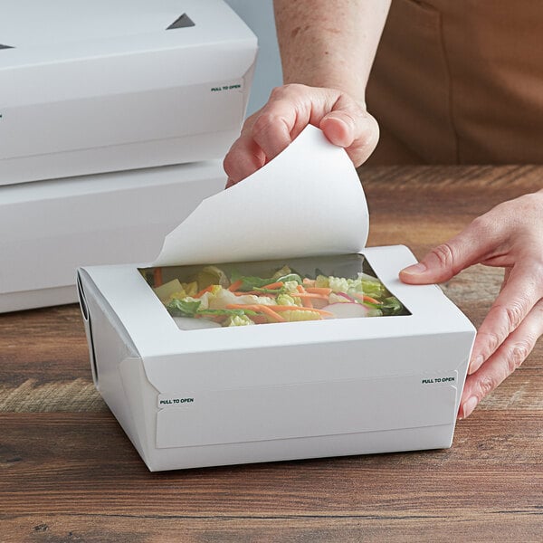 A hand opening a Bio-Pak white paper take-out container with a window