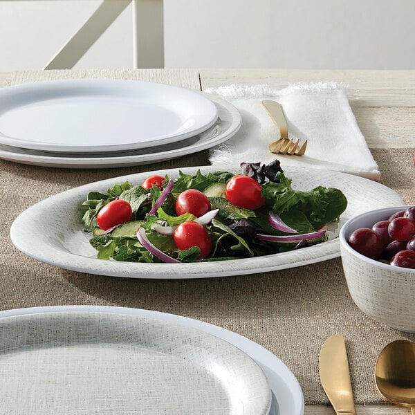 An American Metalcraft Jane Casual oval melamine platter with salad and a bowl of grapes on a table.