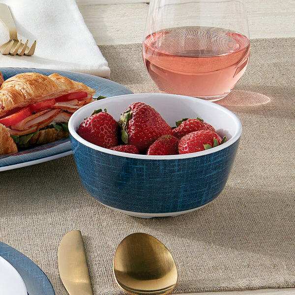 An American Metalcraft denim melamine bouillon cup filled with strawberries on a table with croissants.