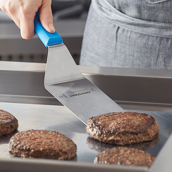 A person using a Dexter-Russell high heat blue hamburger turner to cook hamburger patties.