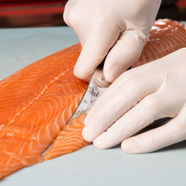 A person in gloves using a Victorinox flexible narrow boning knife to cut salmon.