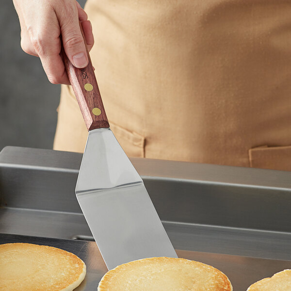 A person using a Dexter-Russell Traditional pancake turner to flip a pancake on a pan.