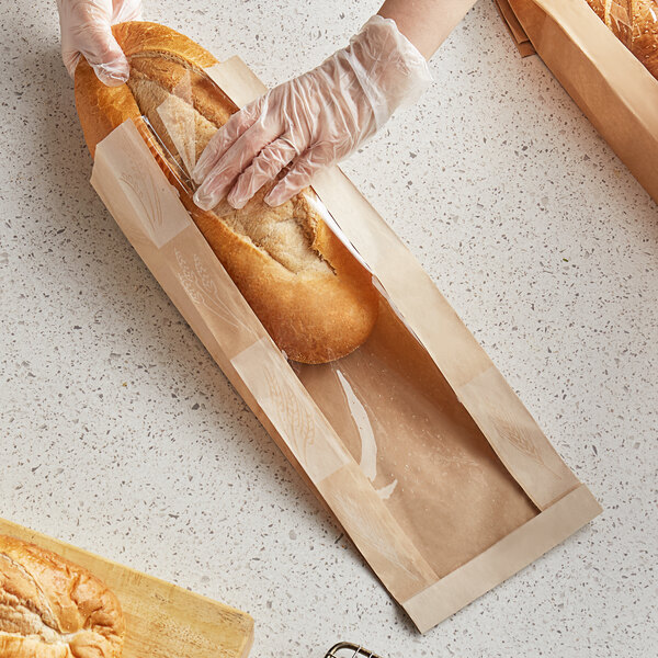 A person in plastic gloves putting a loaf of bread in a Bagcraft Packaging EcoCraft Dubl-Panel bread bag.