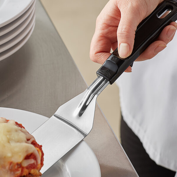 A hand holding a Vollrath small blade turner with a black handle over a plate of food.