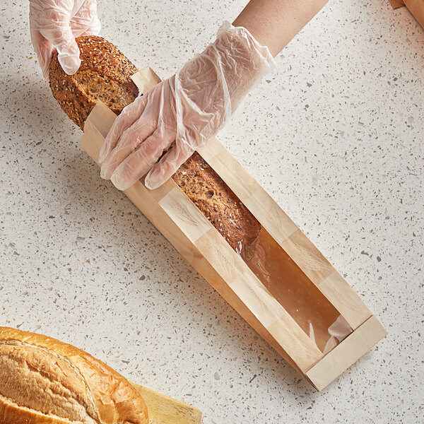 A person wearing plastic gloves putting a loaf of bread in a Bagcraft Packaging paper bag.