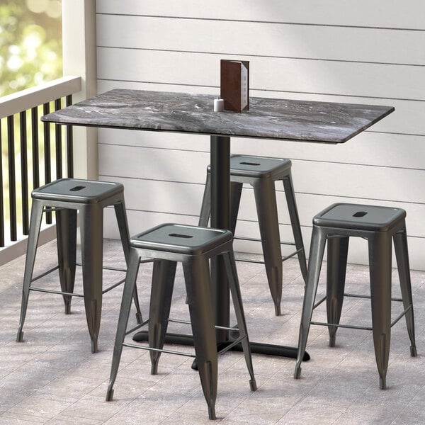 A Lancaster Table & Seating rectangular table with a smooth finish and cross base plate on a porch with black stools.